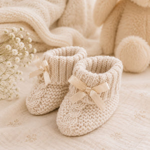 Beige knit baby booties with a little bow and turnover tops