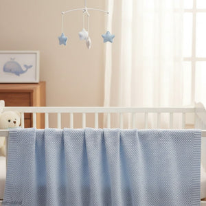 Blue bamboo baby blanket with knitted texture draped over a white cot in a calm nursery