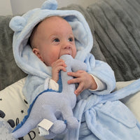 Baby holding the blue knitted diplodocus rattle, with its long neck and darker blue spikes.