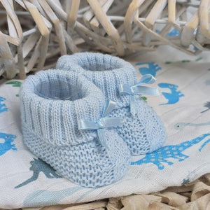 Blue knitted baby booties with ribbon bows on dinosaur-print fabric in a basket