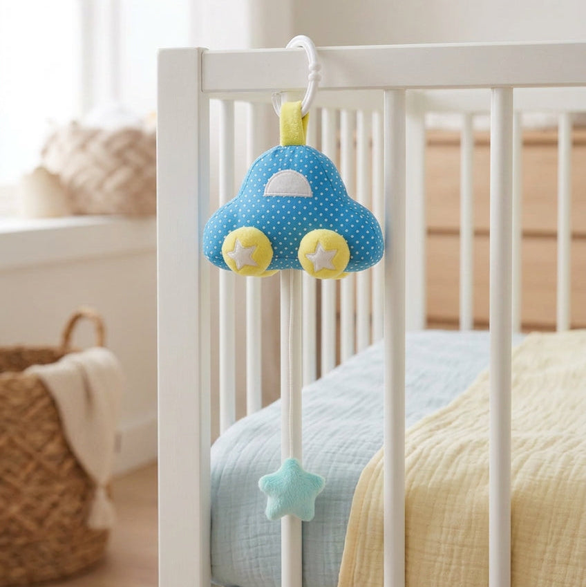 Blue spotted musical car baby toy hanging from a white cot, with star-decorated wheels and a star-shaped pull.