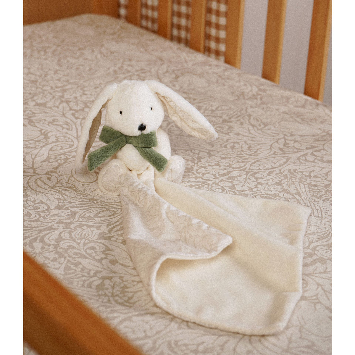 Bunny baby comforter laid on patterned bedding with cream blanket side and folded printed reverse
