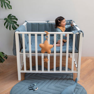 Caramel star pull-down music box hanging from a white playpen, with a coordinating small star below.