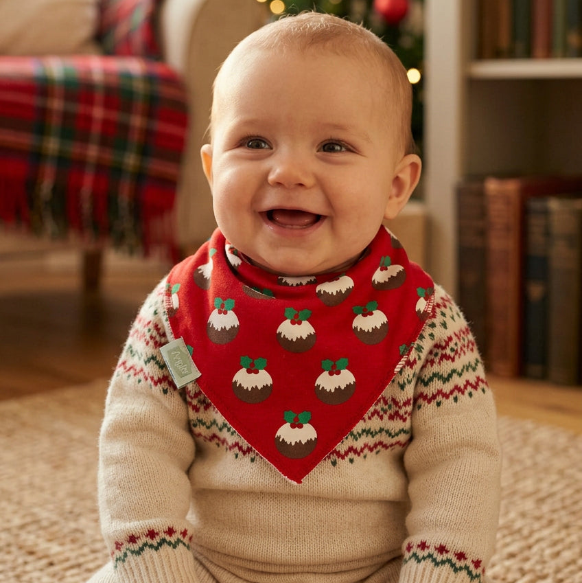 Baby wearing a red Christmas pudding print bandana bib with green trim over a festive jumper.