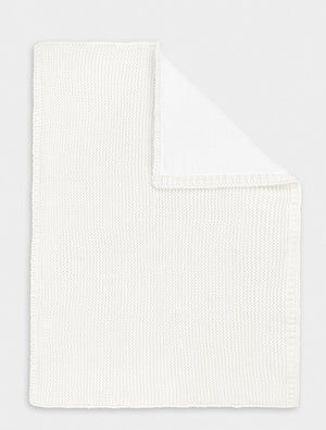 Flat lay of a white cotton knitted baby blanket, a classic newborn essential for nursery or gifting