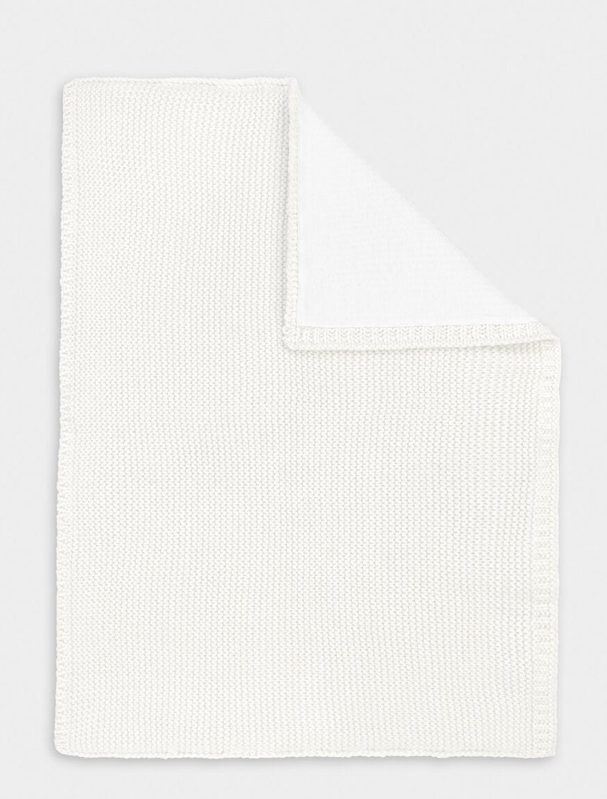 Flat lay of a white cotton knitted baby blanket, a classic newborn essential for nursery or gifting