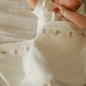 Cream organic baby blanket with embroidered bunny detailing shown with baby.