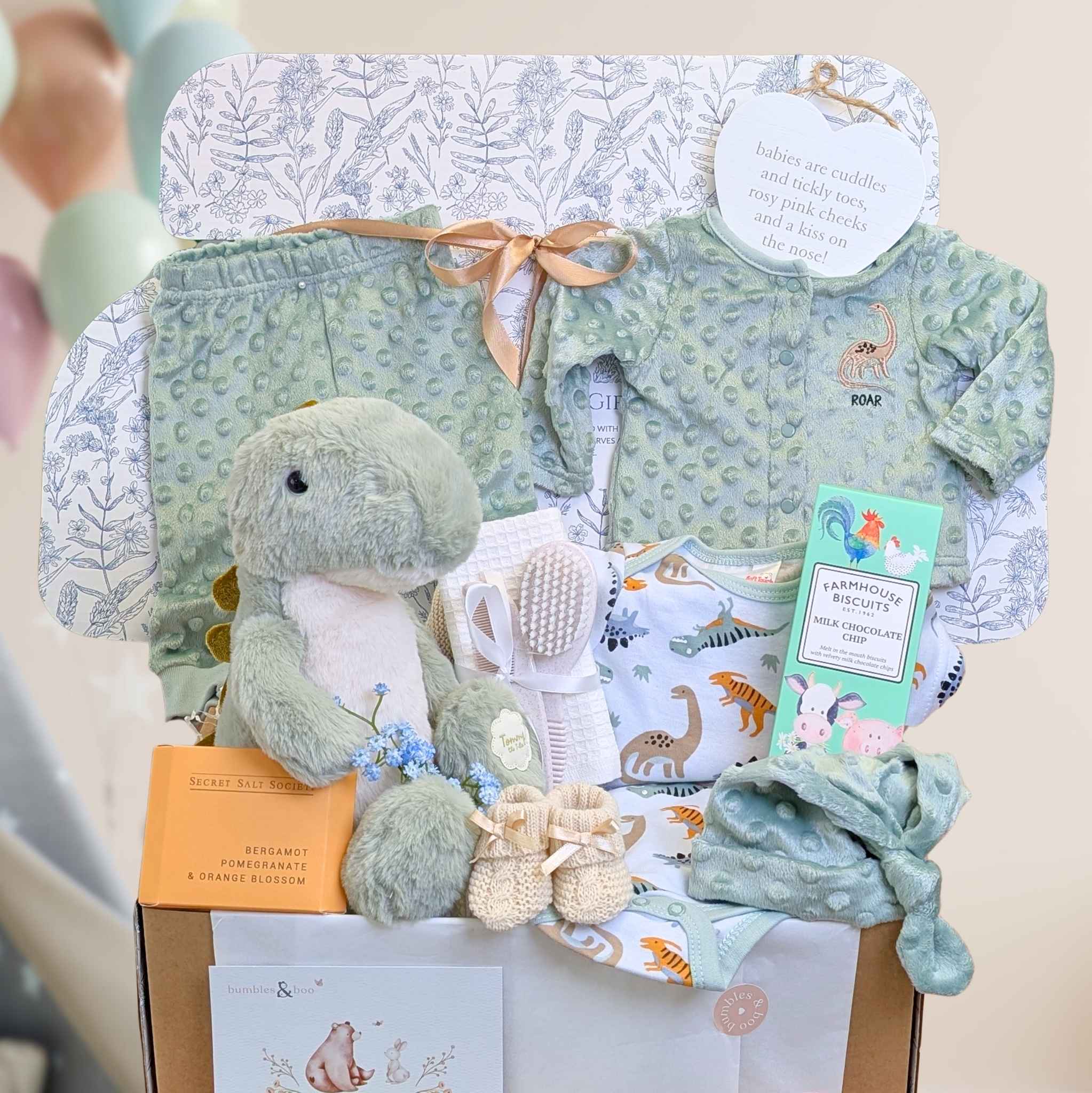 Baby gift set with green plush toy, baby clothes, and other items on a white background