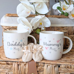Two white mugs labeled 'Daddy's Mug' and 'Mummy's Mug' with baby booties.