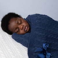Dark blue cable knit baby blanket with bow wrapped around a sleeping baby