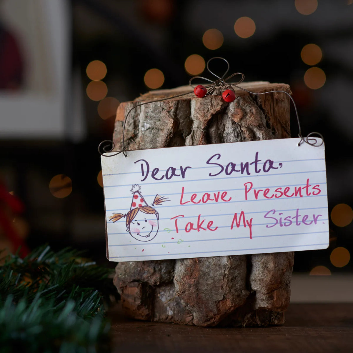 Dear Santa Leave Presents Take My Sister hanging sign with a Santa illustration against a rustic log.