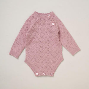 Close up of dusky pink knit baby girl bodysuit with button fastening and textured knit pattern baby clothes detail.