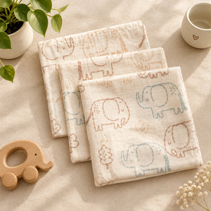 Three folded cream muslin mouth cloths with pastel elephant prints, arranged on a tabletop