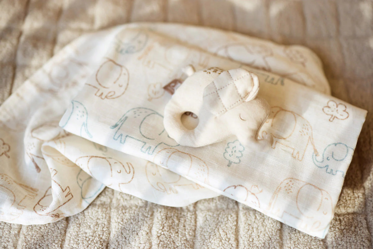Elephant print muslin cloths draped over a soft blanket beside a plush elephant toy