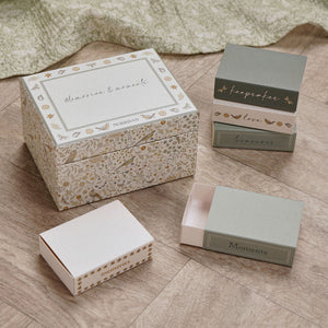 Floral baby keepsake box with labelled matchbox compartments arranged beside it on a wooden surface