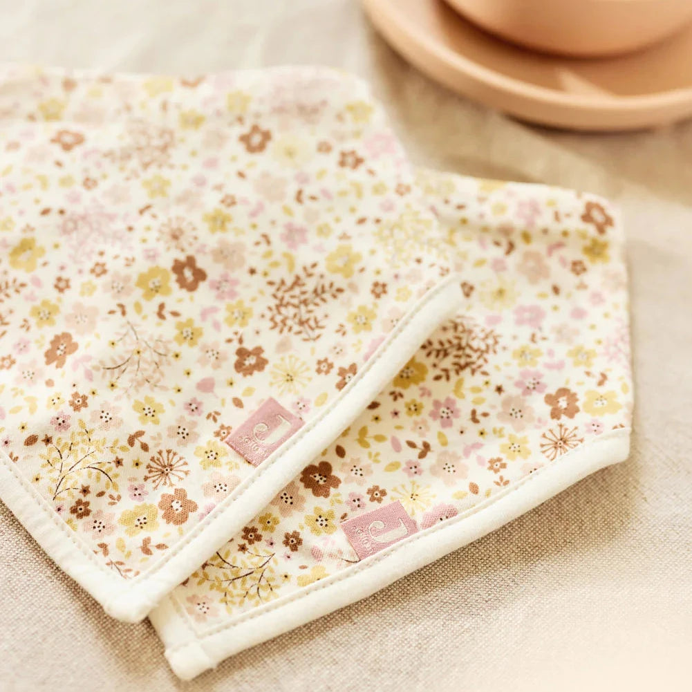 Floral-patterned 2 pack bandana bibs on a beige surface with a bowl of cereal in the background