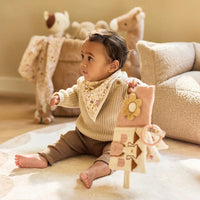 Child playing with a toy in a cozy room with teddy bears and soft furniture wearing flower fairies bib
