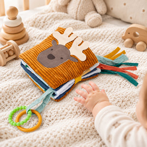 Forest soft baby activity book with a deer cover, fabric ribbons and teething ring beside a baby