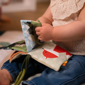Baby holding a page of the forest soft fabric book with a red fox illustration