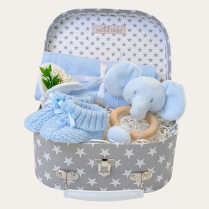 Baby boy gifts hamper with blue elephant toy, knitted booties, and other items in a luggage trunk.
