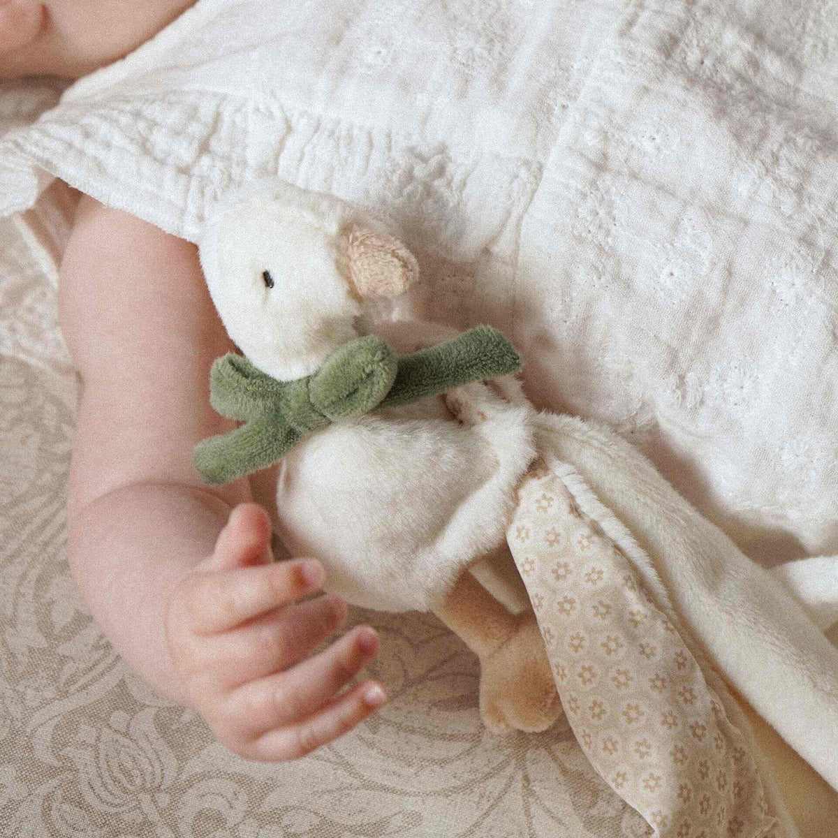 Baby holding the goose comforter with green bow and patterned blanket edge visible