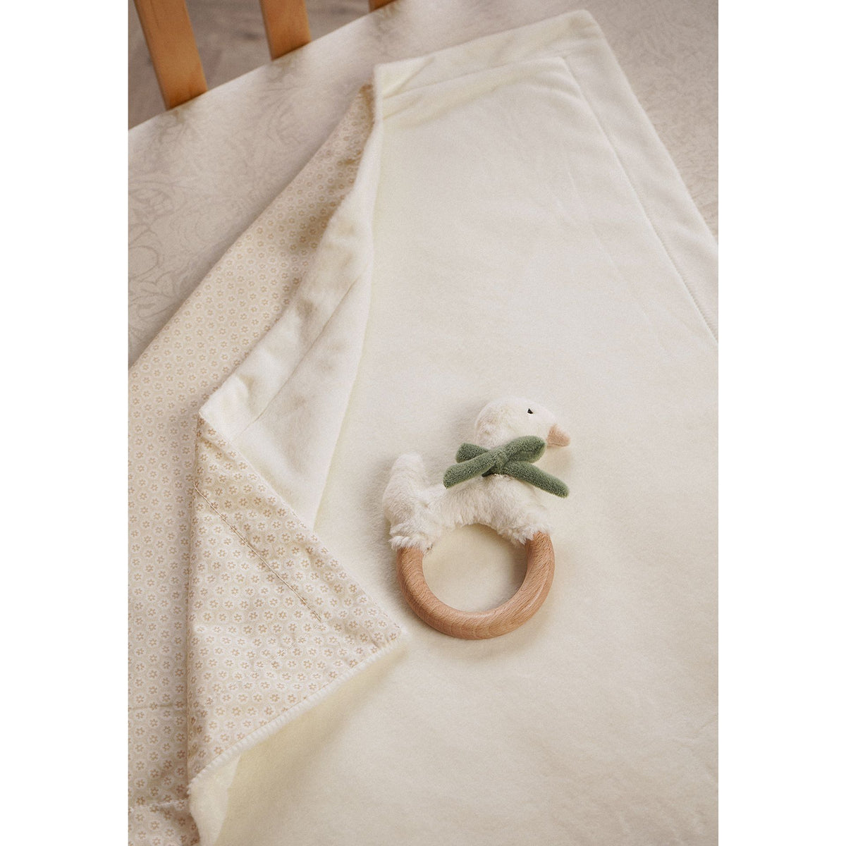 Plush baby blanket draped over a chair with its patterned reverse and goose wooden ring teether visible.