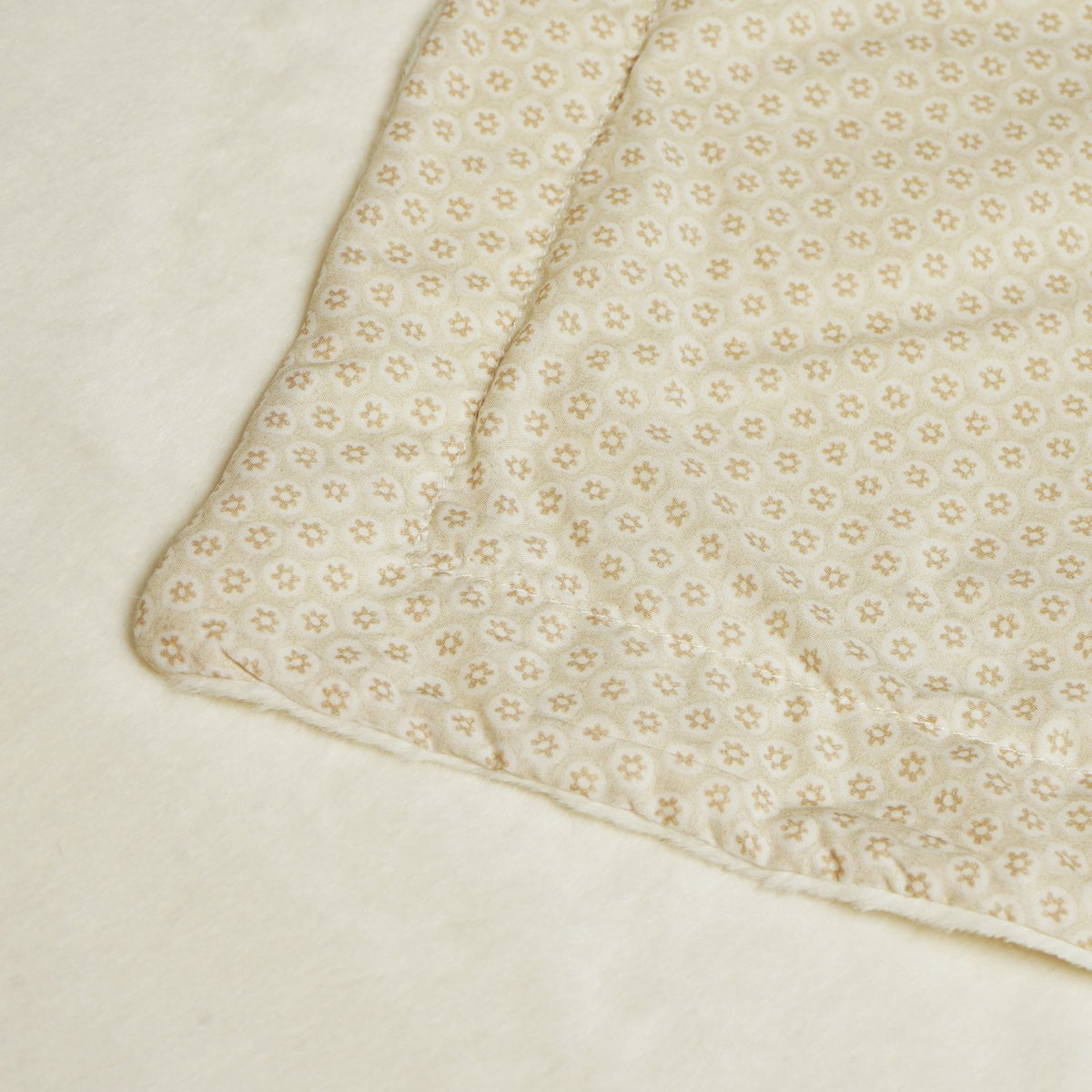 Close-up of the baby blanket’s small floral reverse, stitched edge and plush cream surface.
