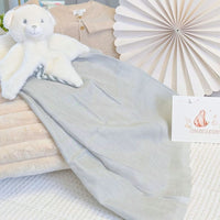 Grey muslin square draped across a display with a soft toy and gift card.