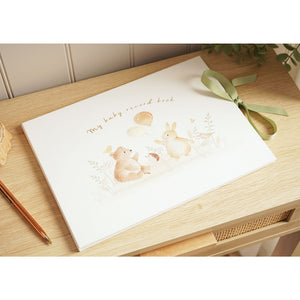 Closed illustrated baby record book on a wooden surface, with a green ribbon tie and animal artwork on the cover.