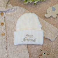 Knitted white baby beanie hat with 'just arrived' embroidered on the front
