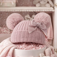Knit pompom hat for a baby girl in dusky pink with a velvet bow.
