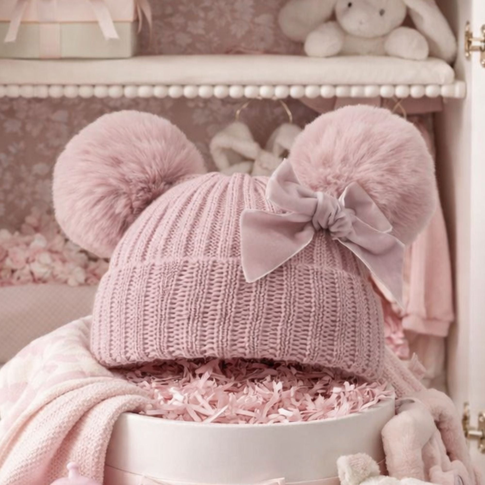 Knit pompom hat for a baby girl in dusky pink with a velvet bow.
