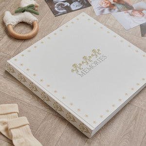 Linen memories album with floral cover beside baby photographs and a wooden ring toy