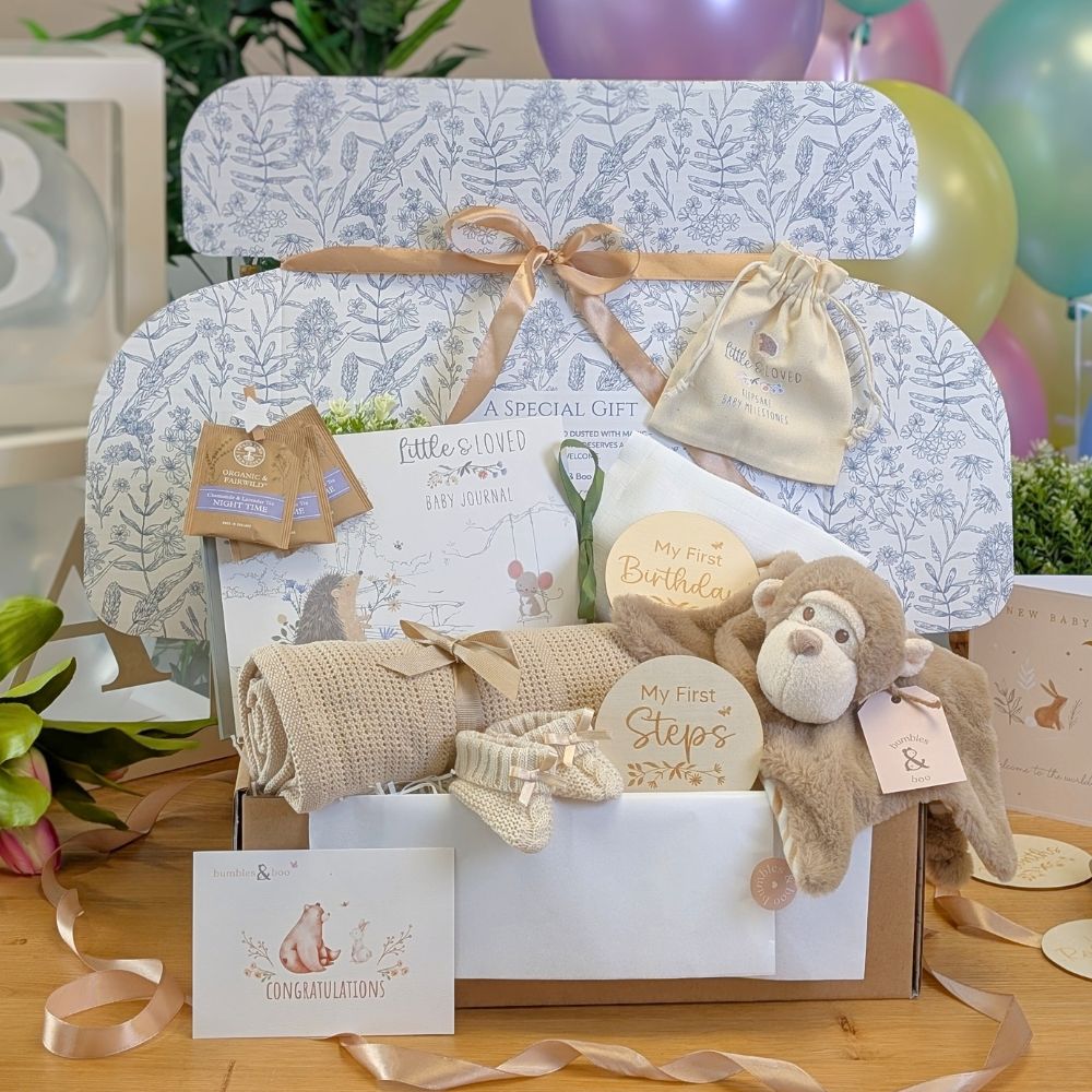 Beige baby hamper with journal, booties, blanket and plush monkey toy.