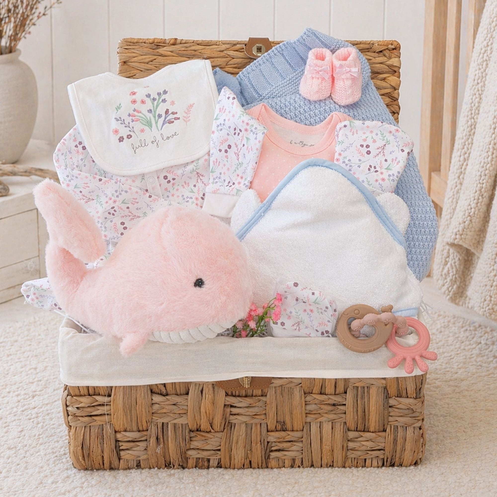 Luxury baby girl hamper basket with newborn gifts including cuddly pink whale soft toy, blue blanket and white towel.