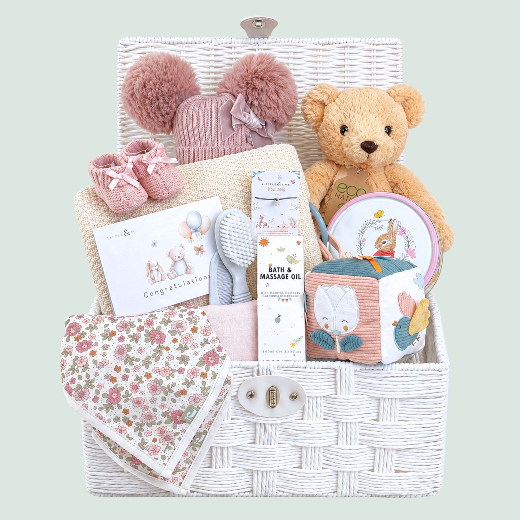 Gifts for a baby girl in a white hamper basket with blanket, teddy bear and an array of presents
