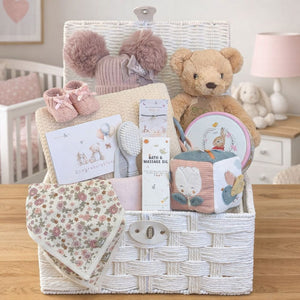Gifts for a baby girl in a white hamper basket with blanket, teddy bear and an array of presents