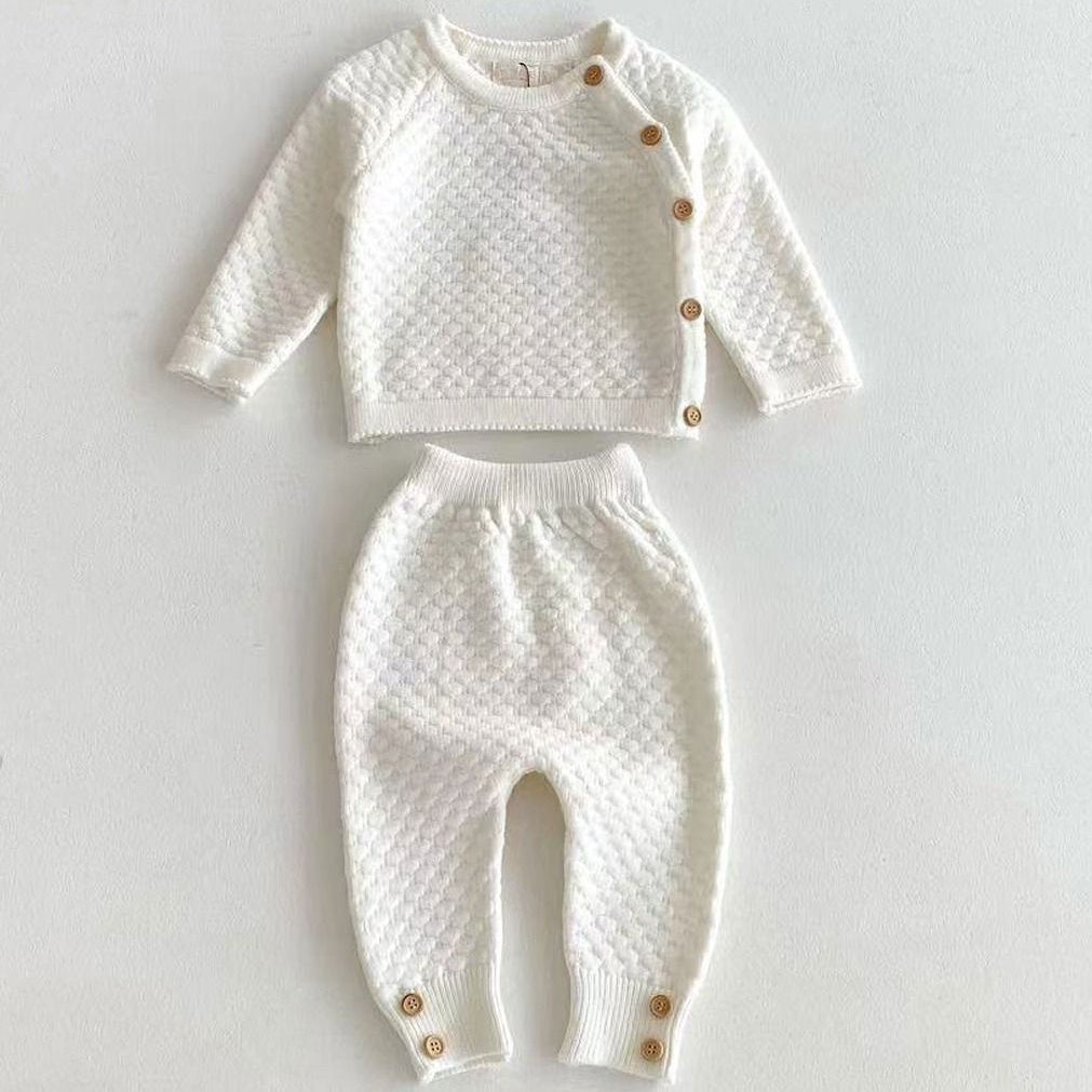Luxury ivory knitted baby clothes set with textured honeycomb knit top and trousers laid flat showing button details
