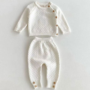 Luxury ivory knitted baby clothes set with textured honeycomb knit top and trousers laid flat showing button details