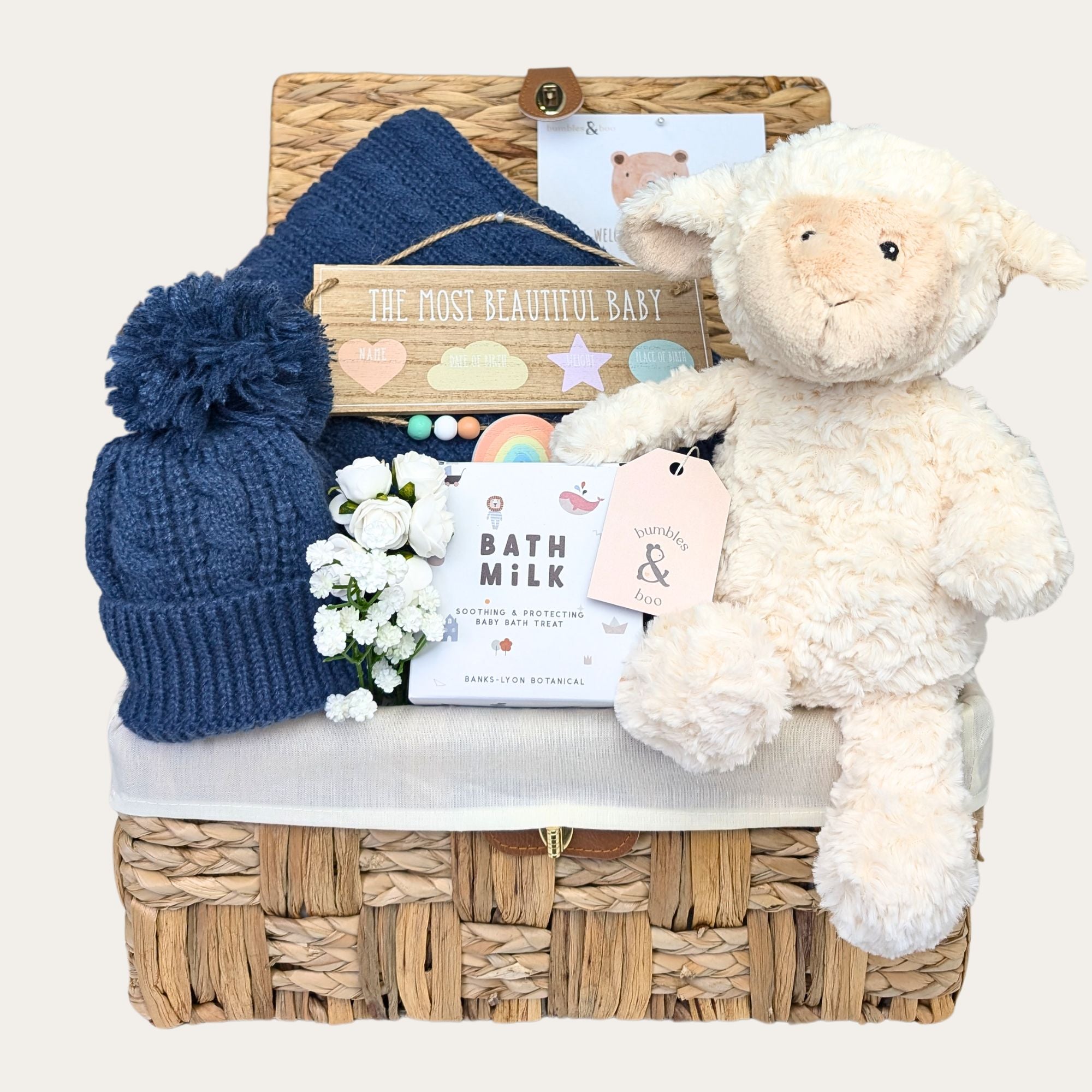 Baby boy hamper basket with gifts including white lamb soft toy and dark blue pom pom hat. Bumbles and Boo.