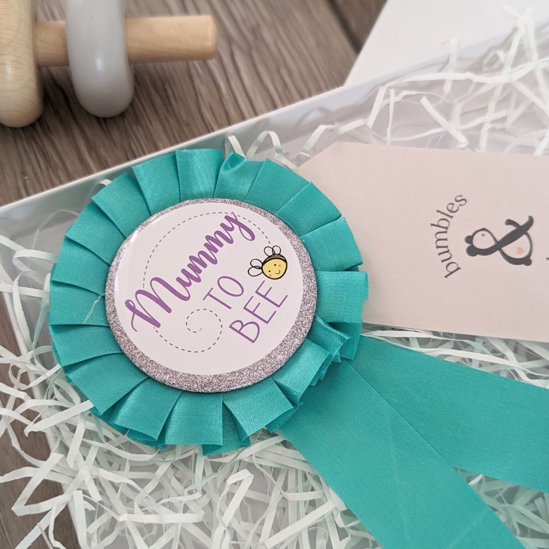 Baby hamper gift which fits perfectly through the letterbox. Beautifully designed with a pair of baby booties, countdown plaque, baby mittens and badge for Mummy to bee.