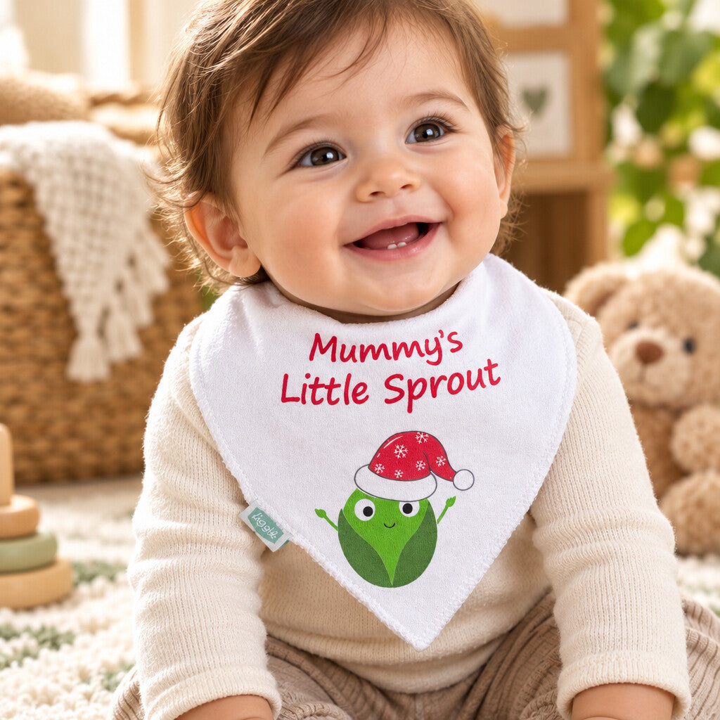 Baby wearing a white bandana bib printed with “Mummy’s Little Sprout” and a green sprout in a red Santa hat.