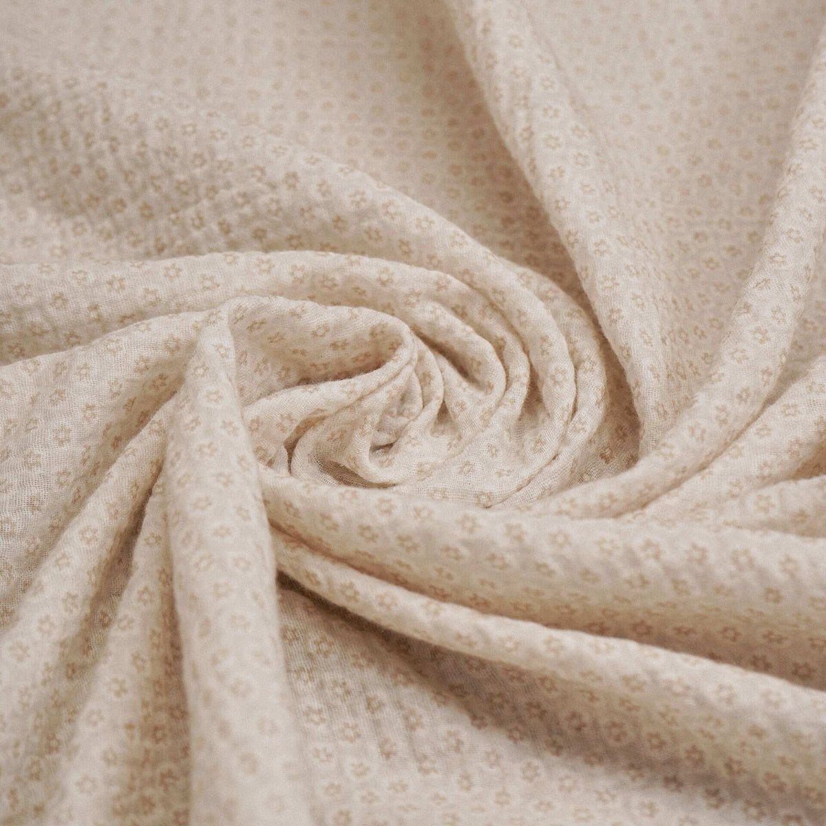 Natural baby muslin cloth with a small repeating floral pattern arranged in soft folds.