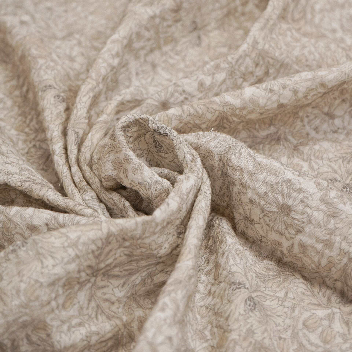 Natural-toned baby muslin fabric showing its detailed leafy print in a folded close-up.