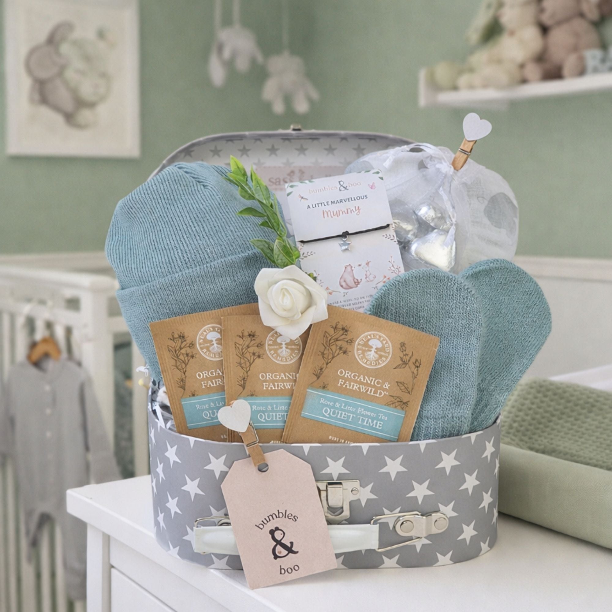 Newborn baby boy gift hamper with sage green knit hat and mittens in a grey suitcase with star pattern.