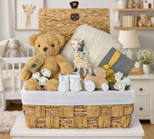 A baby gift hamper with presents including a teddy bear and baby blanket in neutral tones