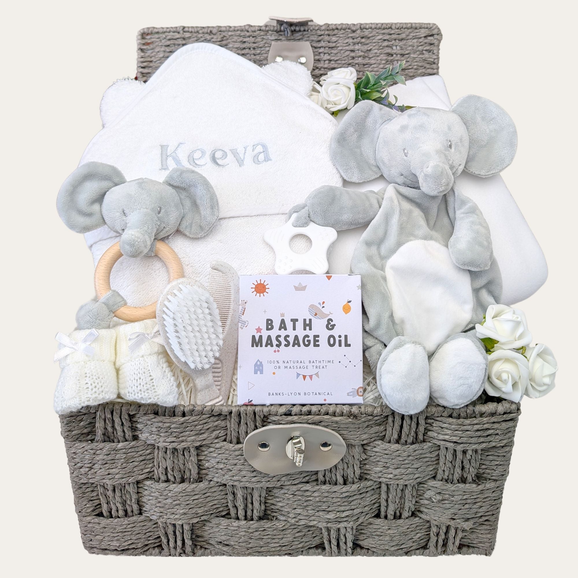 New baby gifts in a hamper basket with white and grey presents for a newborn. Includes personalised towel and elephant toys. 