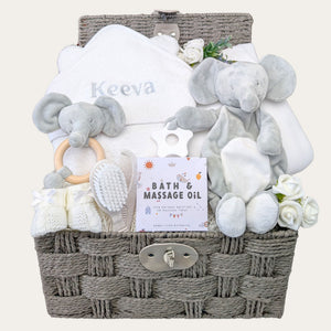 New baby gifts in a hamper basket with white and grey presents for a newborn. Includes personalised towel and elephant toys. 