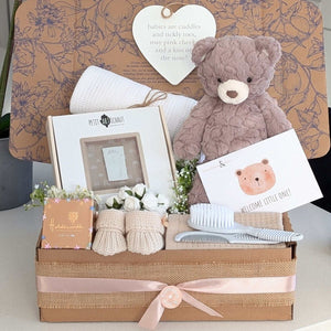 New baby gifts in a box with teddy bear, footprint frame and baby booties.