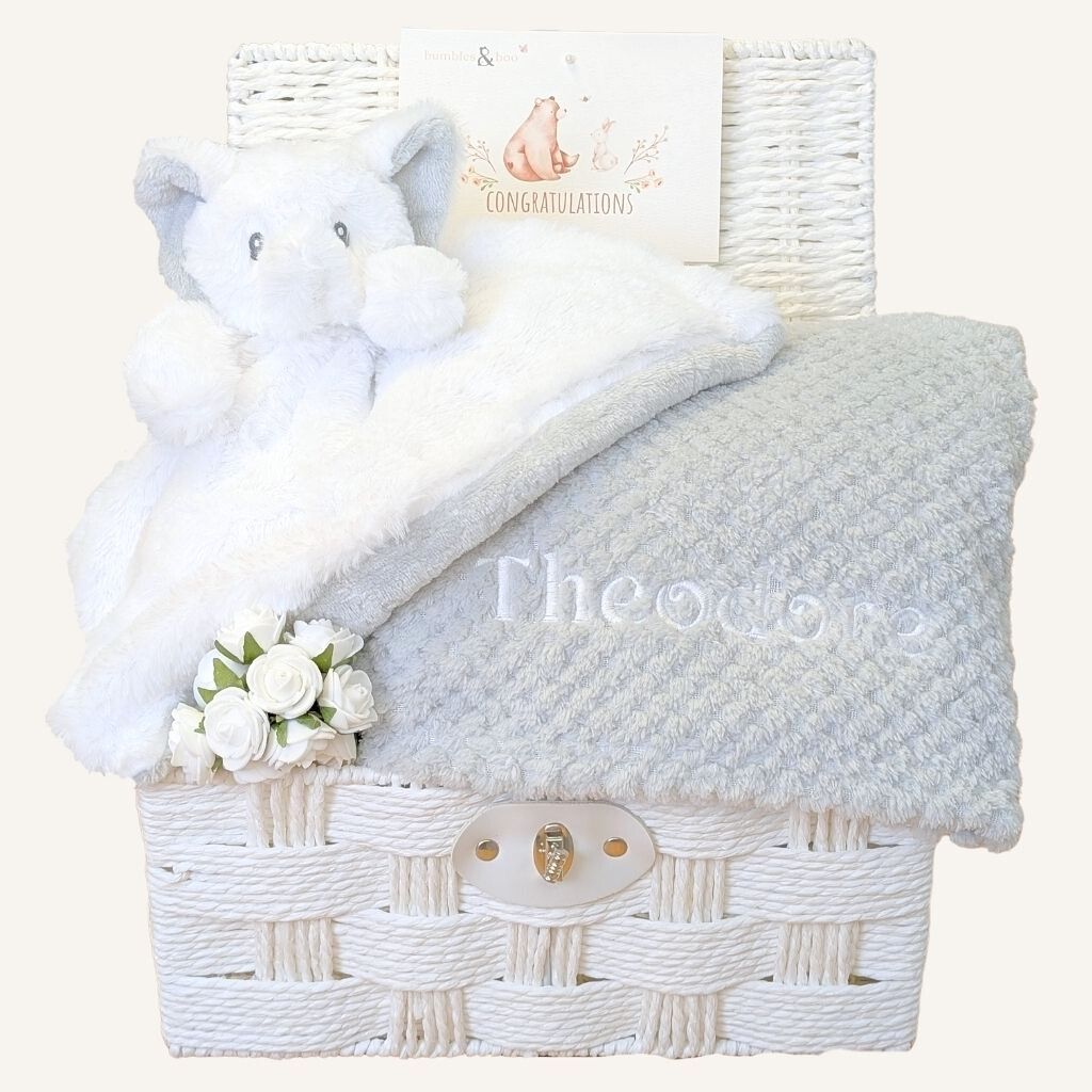 White wicker baby gift hamper basket with gifts including plush toys and a grey blanket 